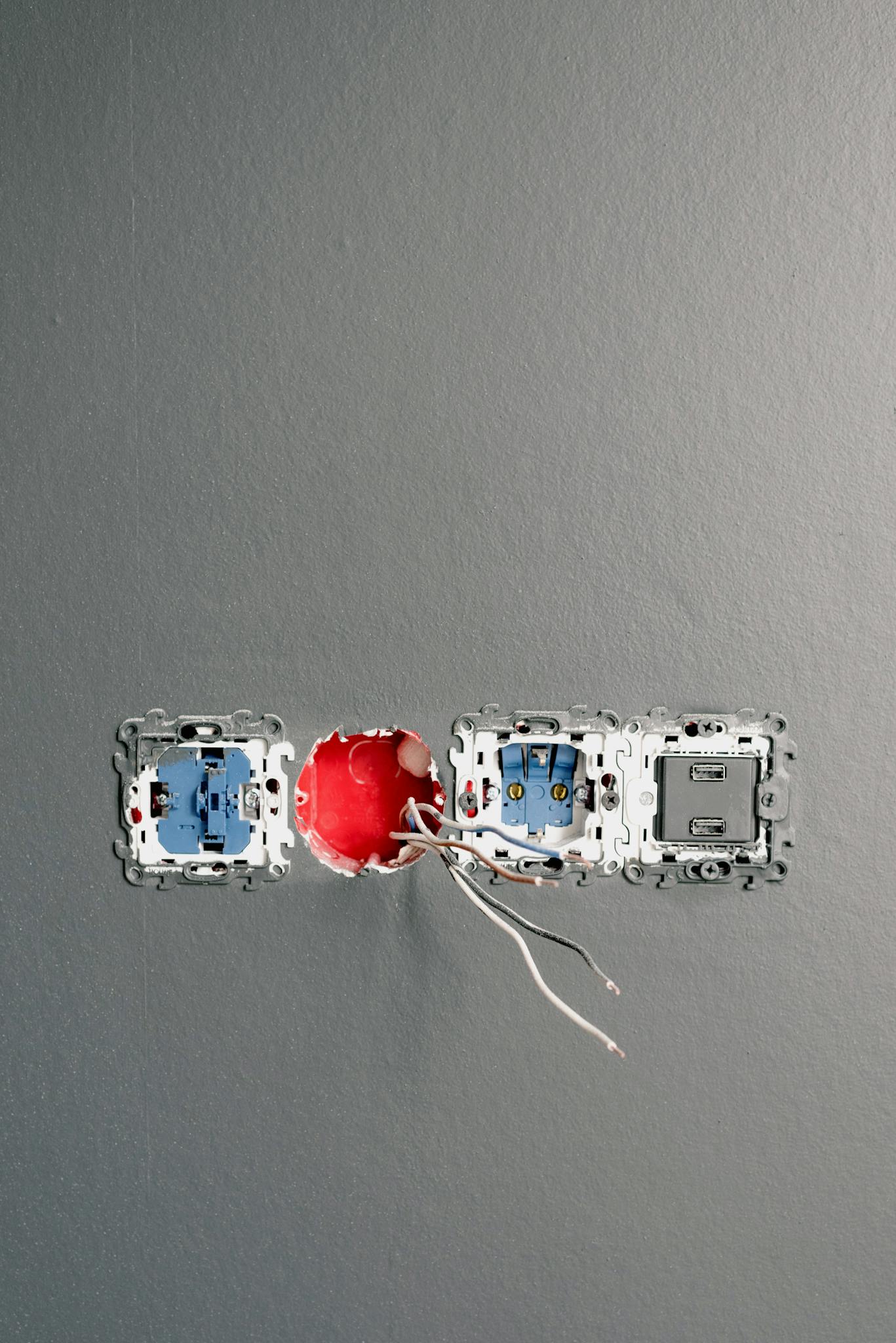 Sockets with wires and bolts on gray painted wall at home during construction